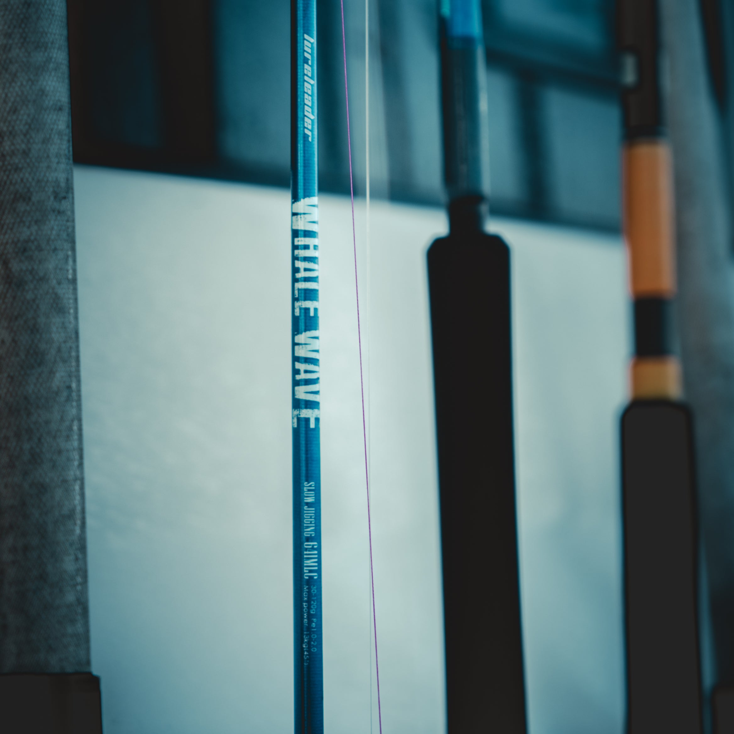 A close-up shot of Lureleader 25 Whale Wave series’ slow jigging rod with a thin pink line, standing vertically against a cool-toned, blurred background.