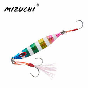 A Mizuchi metal swimbait fishing lure with a multicolor striped body, a blue eye detail, and two treble hooks with orange and pink skirt accents, shown on a plain white background with the Mizuchi brand logo in the top left corner.