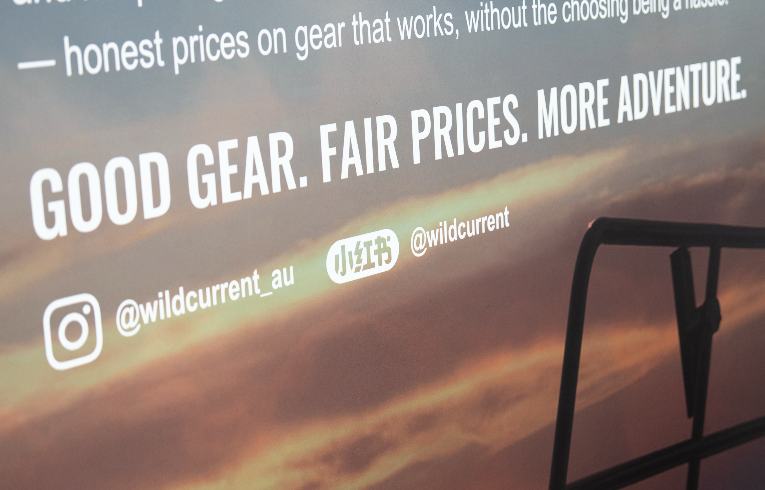A close-up of a printed or projected poster with large white text reading 'GOOD GEAR. FAIR PRICES. MORE ADVENURE.